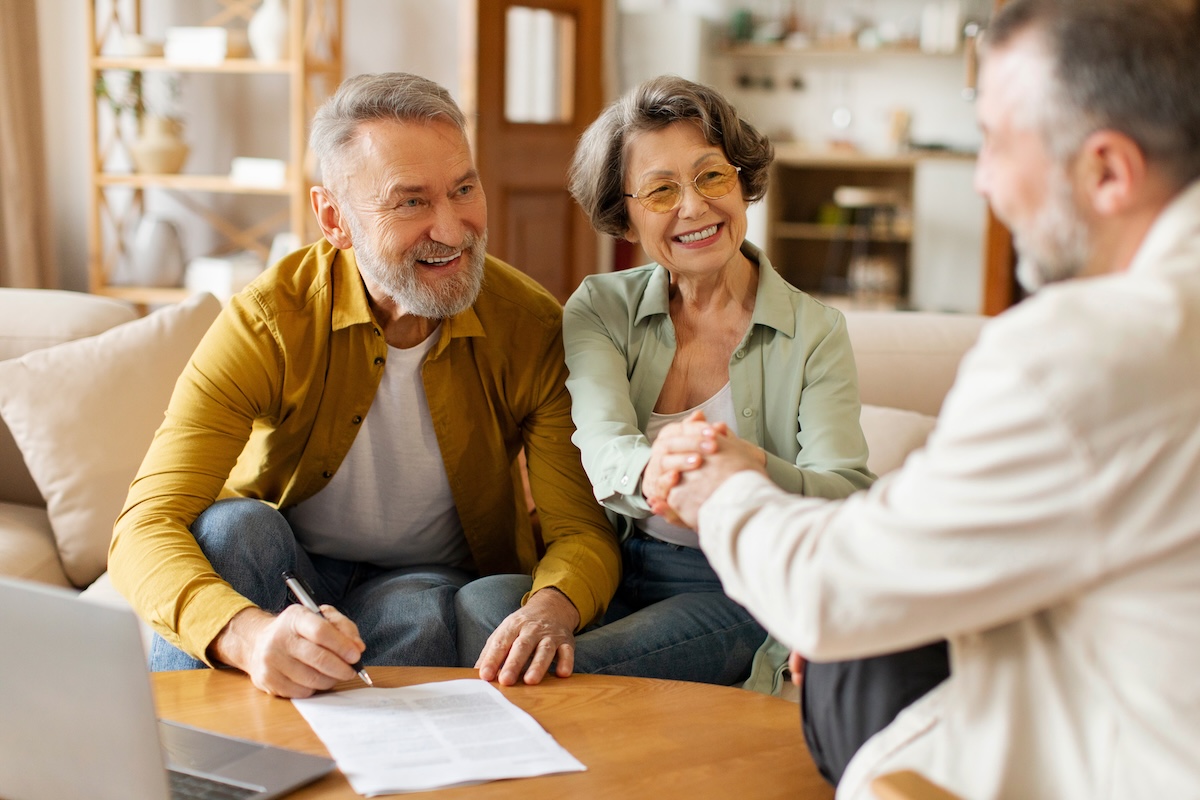 Happy senior couple of clients meeting with real estate agent, shaking hands with contractor and thanking for consultation