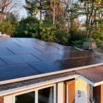 A brick house with a roof covered in solar panels showcases the power of solar energy. Trees and a clear sky are visible in the background, debunking myths about aesthetics and functionality.