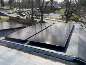 Solar panels installed on a flat rooftop capture solar energy, surrounded by bare trees and overlooking a residential street.