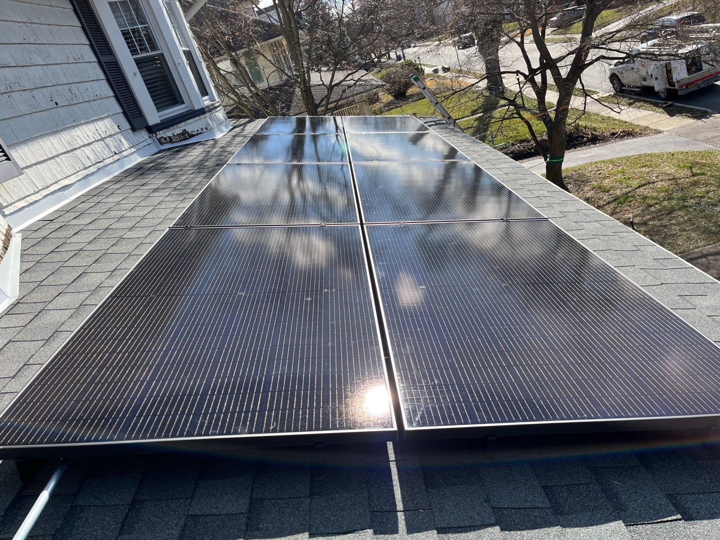 Solar panels efficiently installed on a residential roof reflect sunlight, enhancing energy use. A tree and a utility truck, likely for maintenance, are visible in the background.