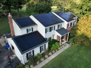 Aerial view of a two-story house with solar panels on the roof, surrounded by green trees and a well-maintained yard—showcasing how easy it is to go solar and benefit from a federal incentive.